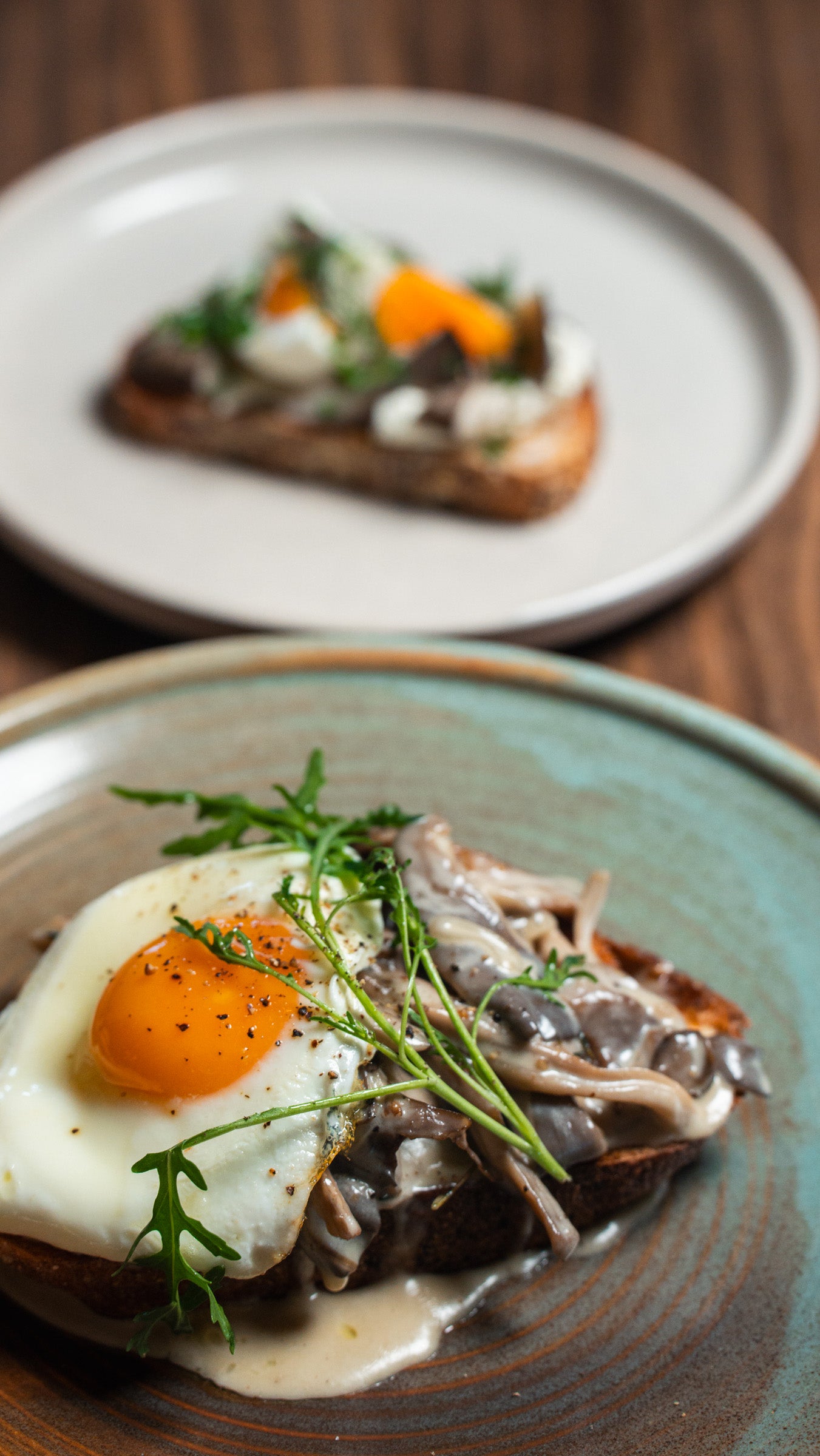 Two plates of food with toast and egg on a wooden table